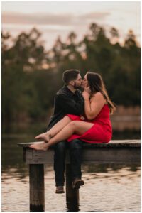 Engagement portrait of couple kissing while seated on a dock at sunset by Coastal Chic Studios