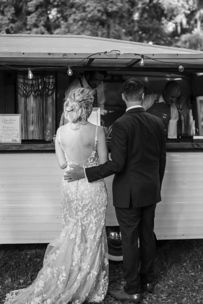 Bride and groom ordering drinks at a vintage trailer bar during a South Carolina wedding reception.