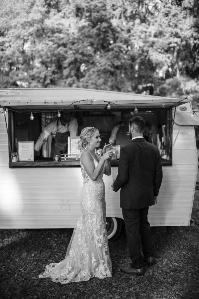Bride and groom ordering drinks at a vintage trailer bar during a South Carolina wedding reception.