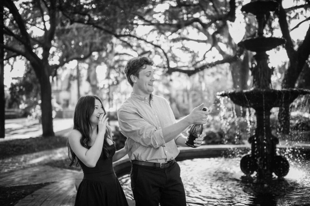 Couple popping champagne near fountain at Lafayette Square in Savannah GA.
