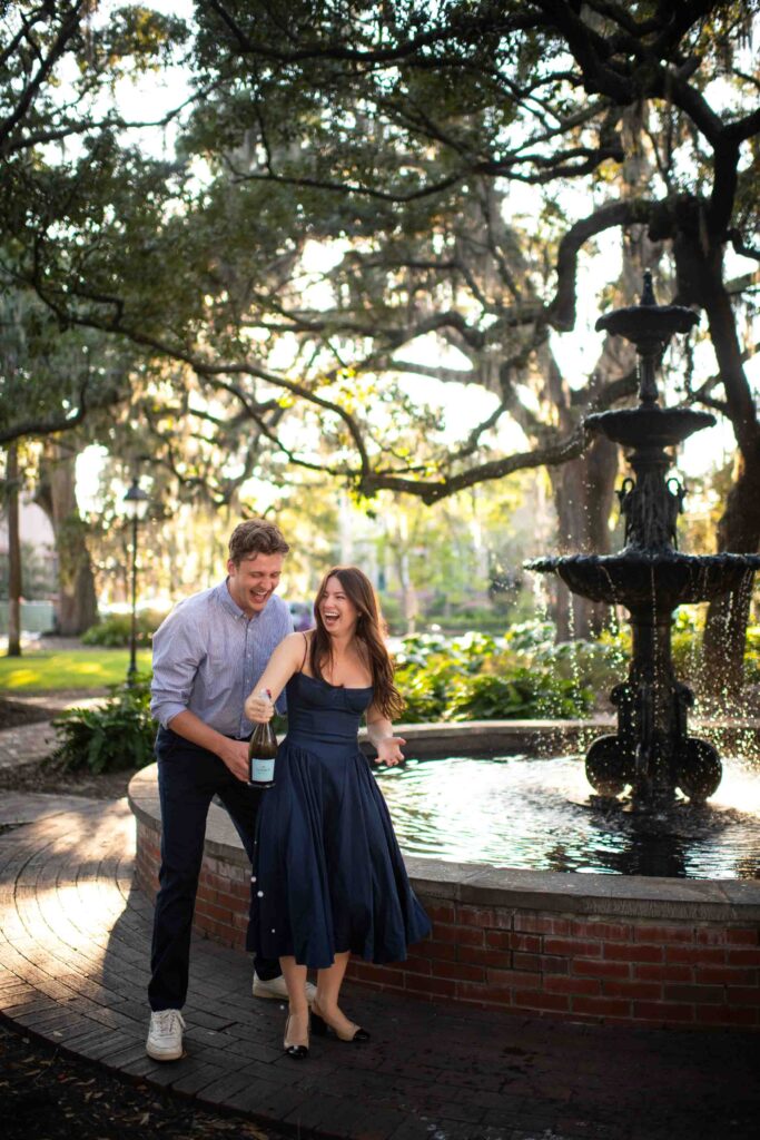 Couple popping champagne near fountain at Lafayette Square in Savannah GA.